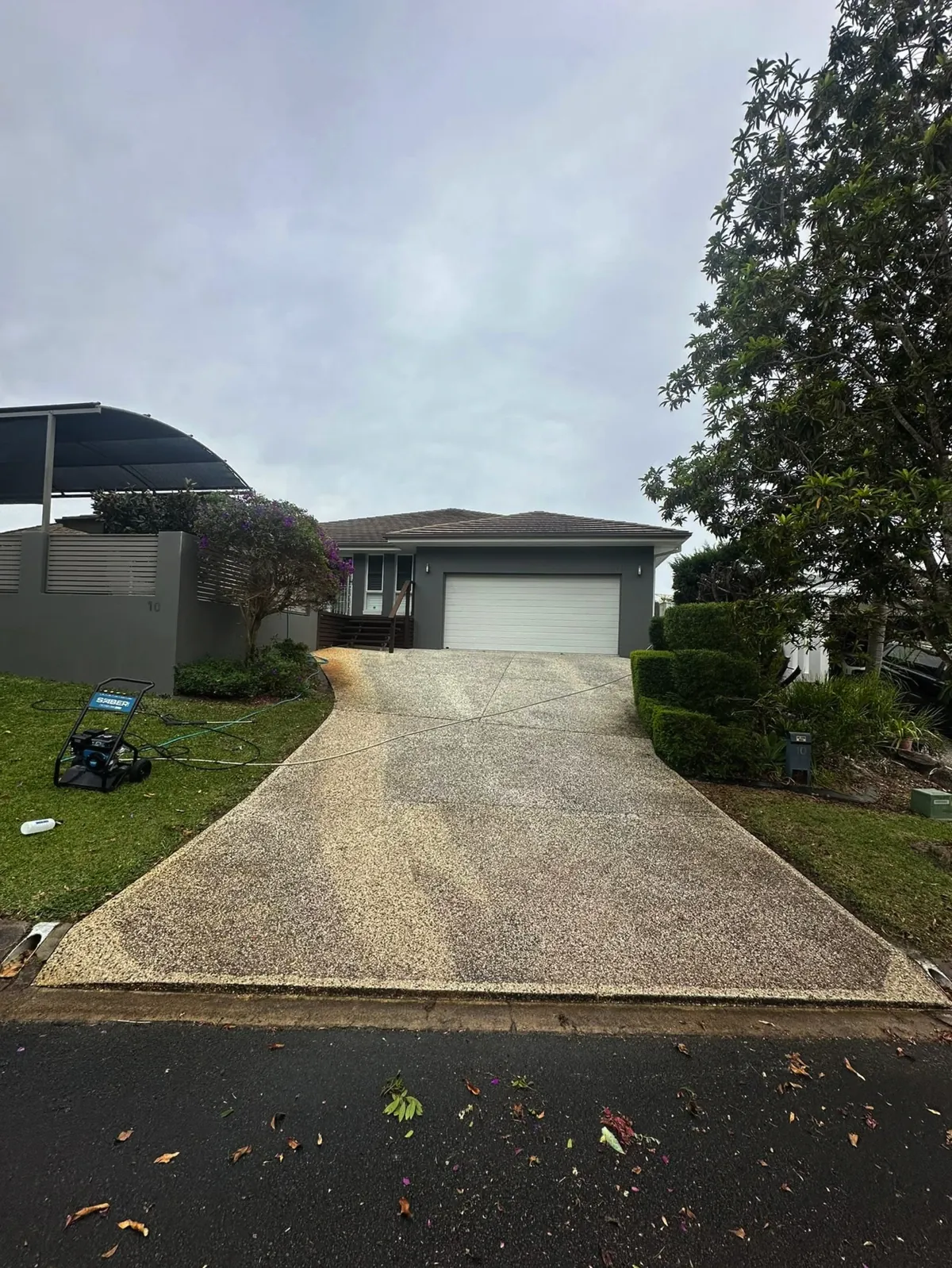 The same driveway before cleaning, grey and stained, with the pressure washer set up on the lawn