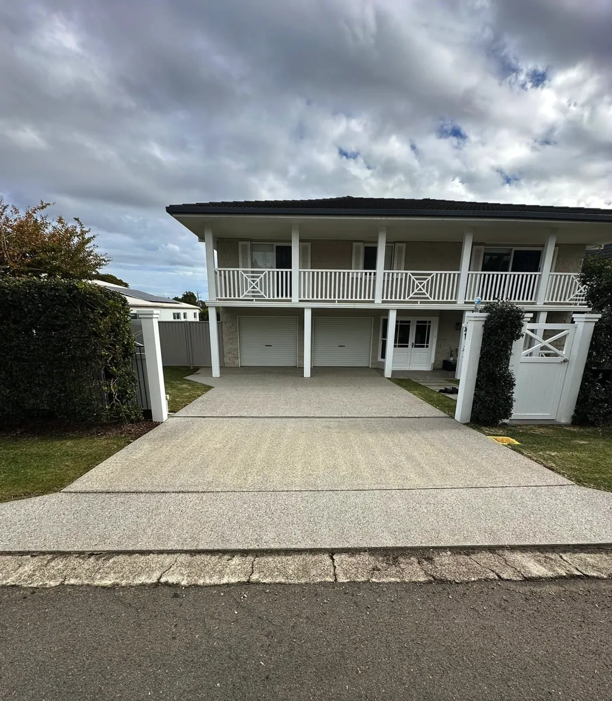 A long concrete driveway cleaned to an even finish in front of a two-storey home