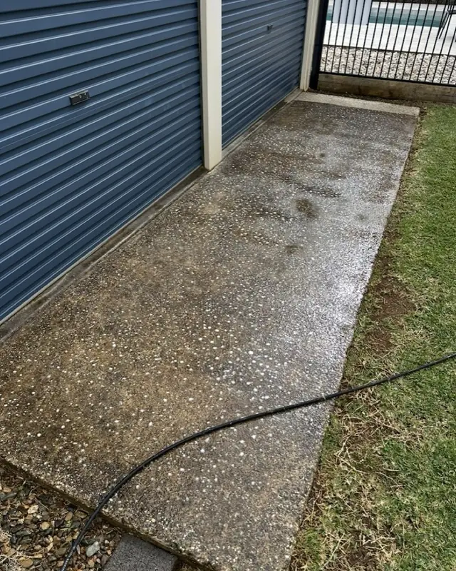 An exposed aggregate slab mid-clean, the washed side reading light and even against the untouched side