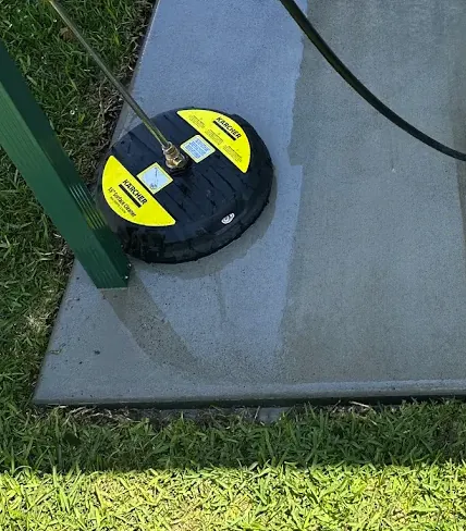 A surface cleaner halfway across a concrete slab, the cleaned section noticeably lighter